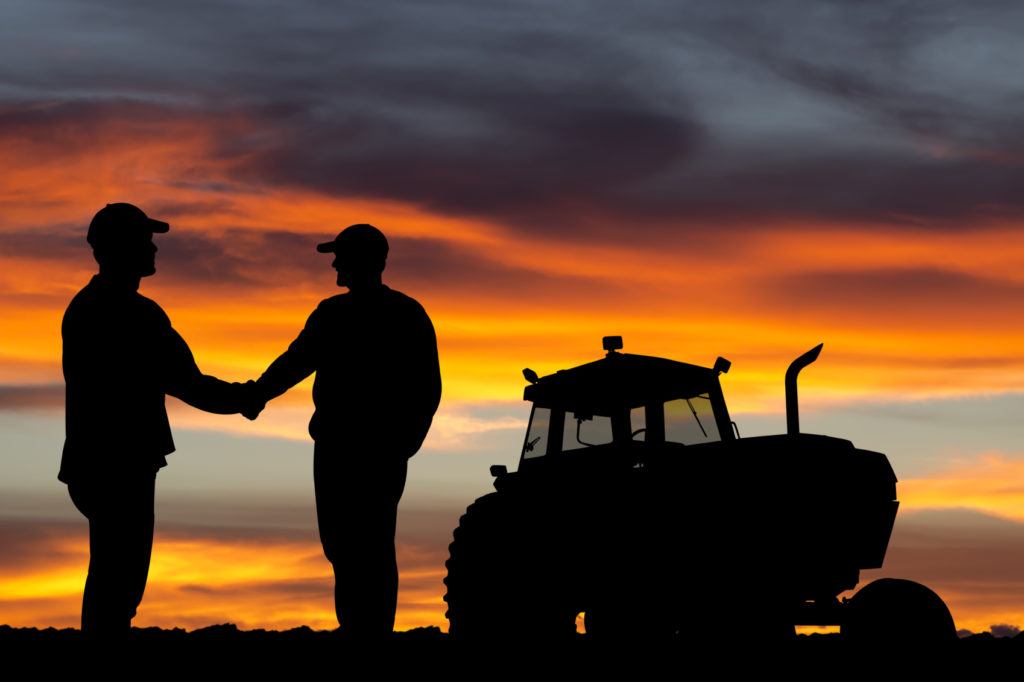A royalty free image from the agriculture industry of two farmers shaking hands at sunrise.